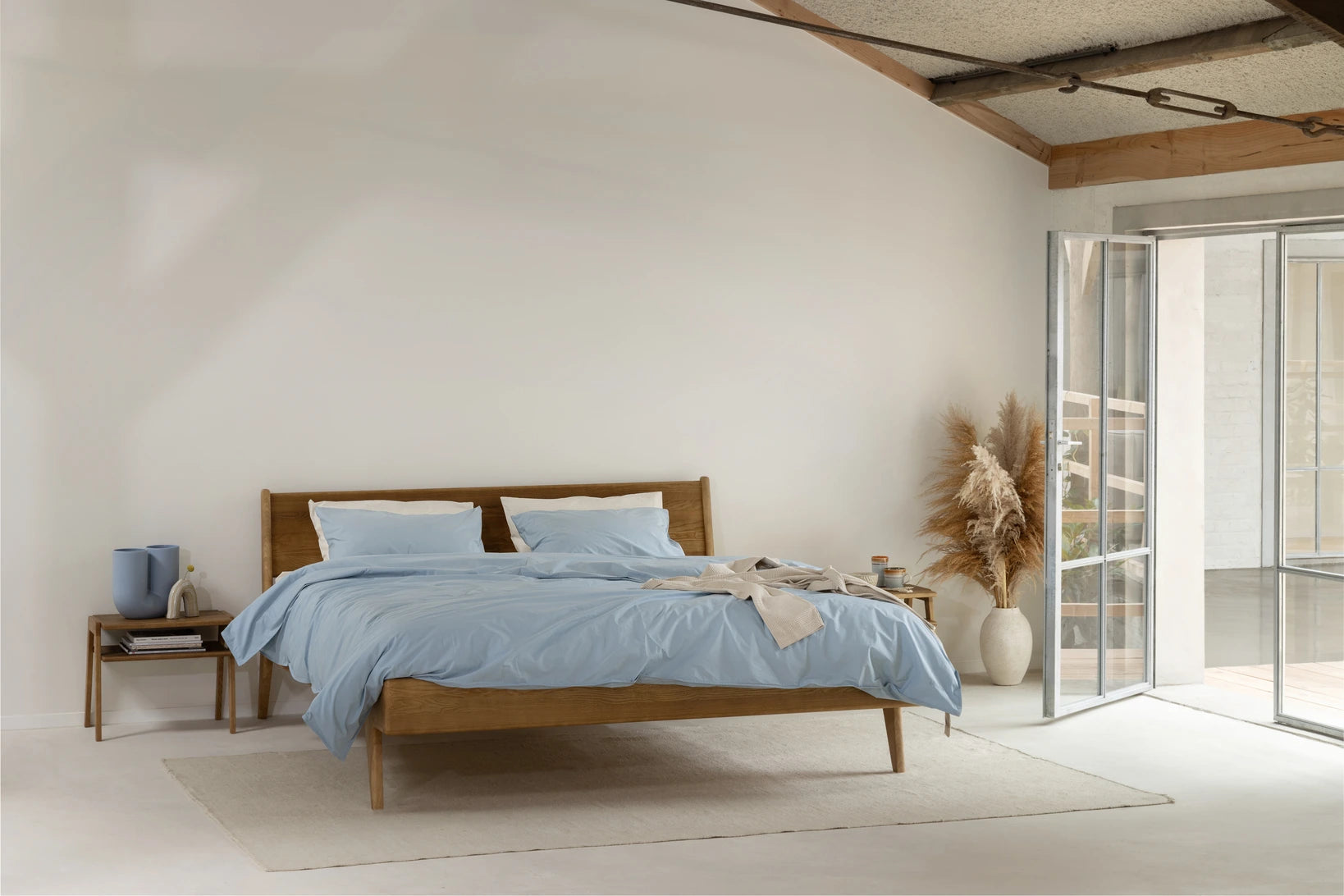 Greensleep bed met massief houten frame en lichtblauwe beddengoed in een lichte, minimalistische slaapkamer